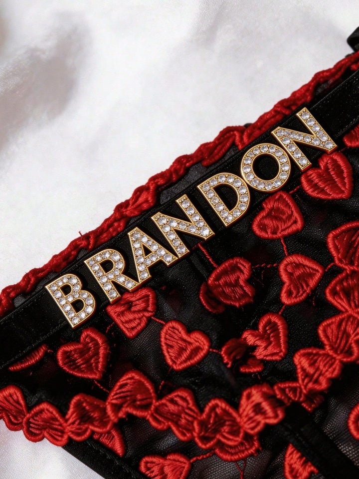 Close-up detail of rhinestone letters and red heart embroidered lace on black mesh underwear